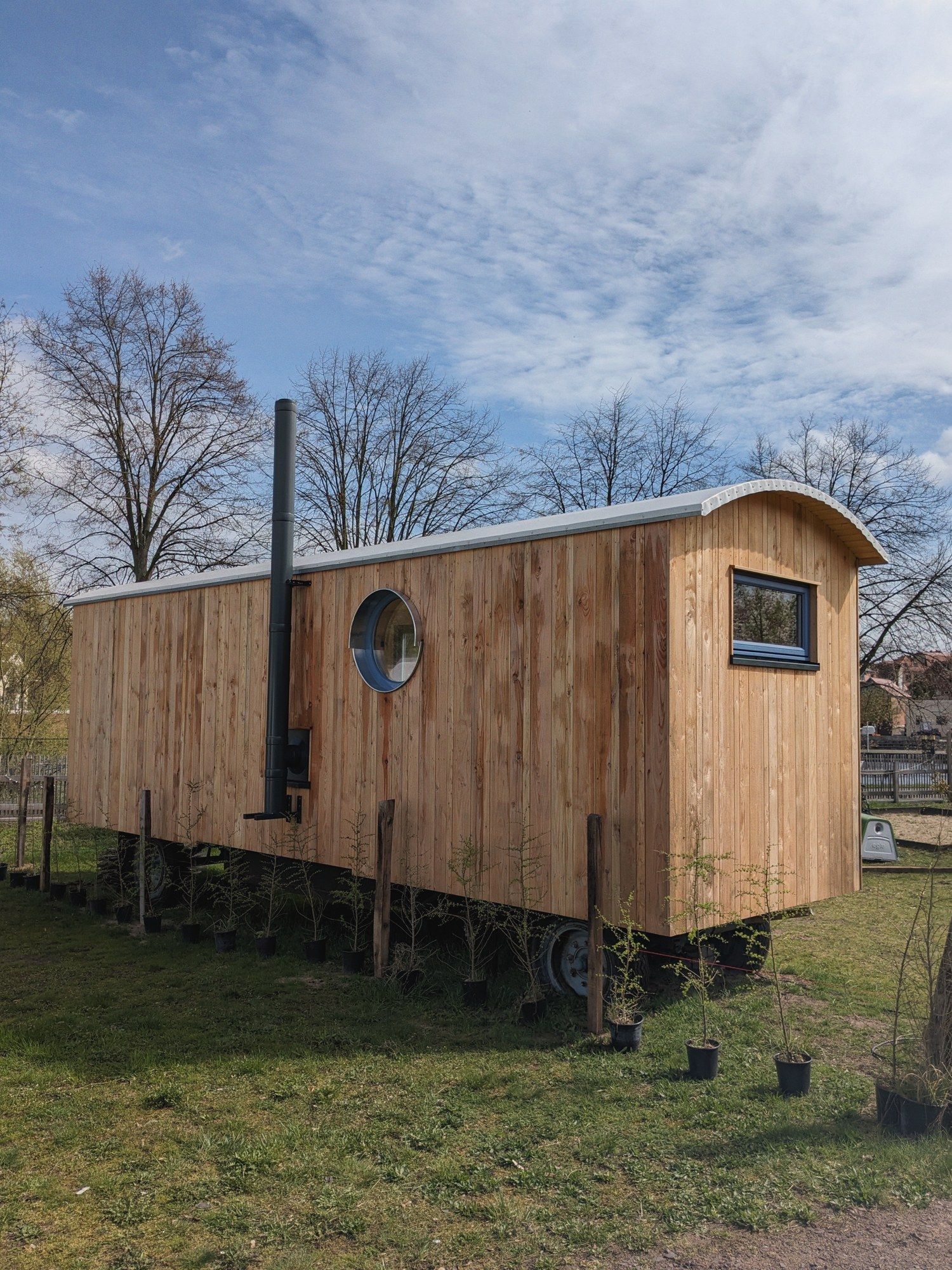 Langer LandAnker aus heller Lärche mit Rundfenster und Ofenrohr, auf altem Fahrgestell im Garten