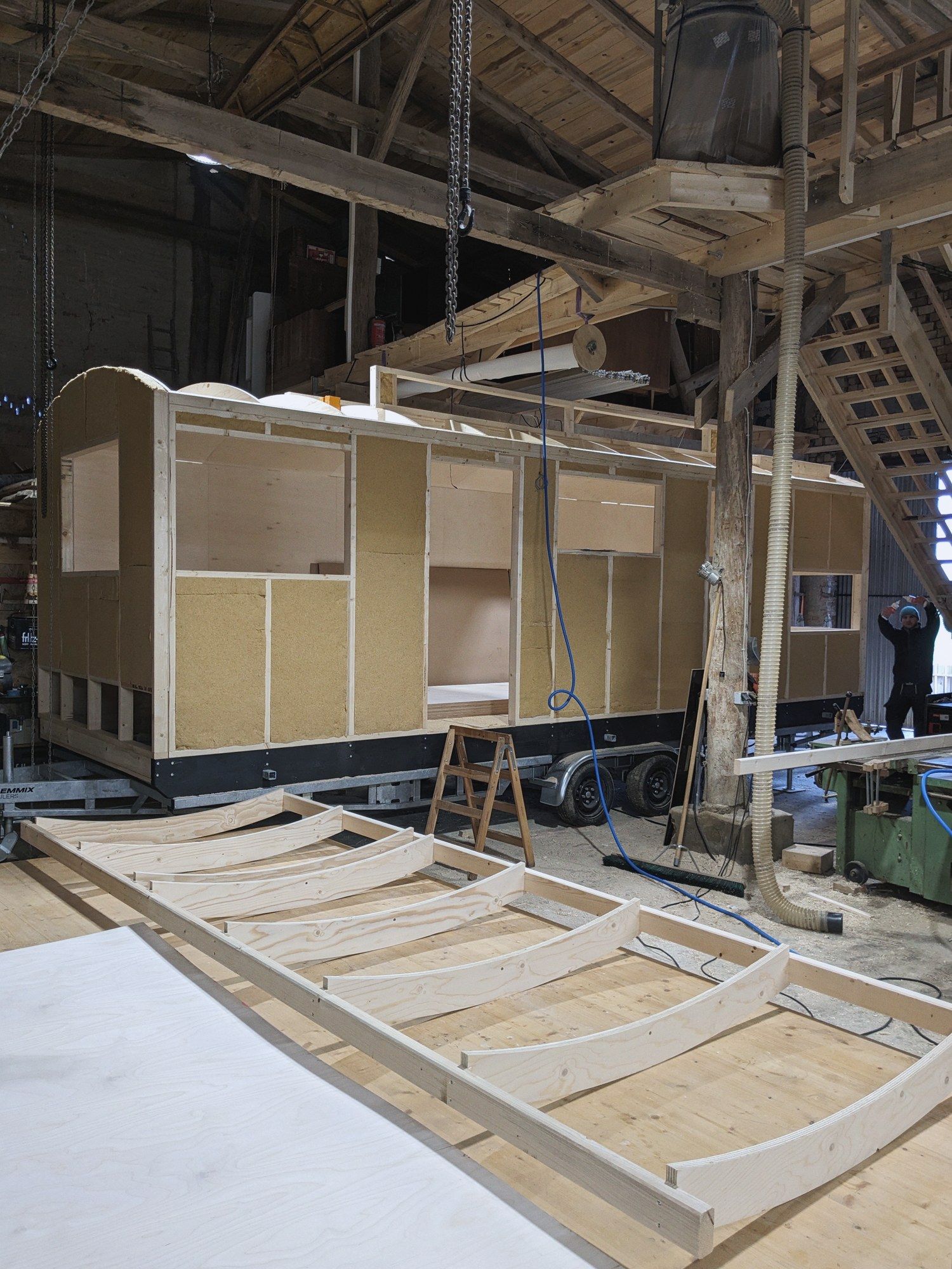 Vorgefertigte Dachbögen auf dem Hallenboden, dahinter ein Rohbau mit Holzfaserdämmung zwischen den Ständern