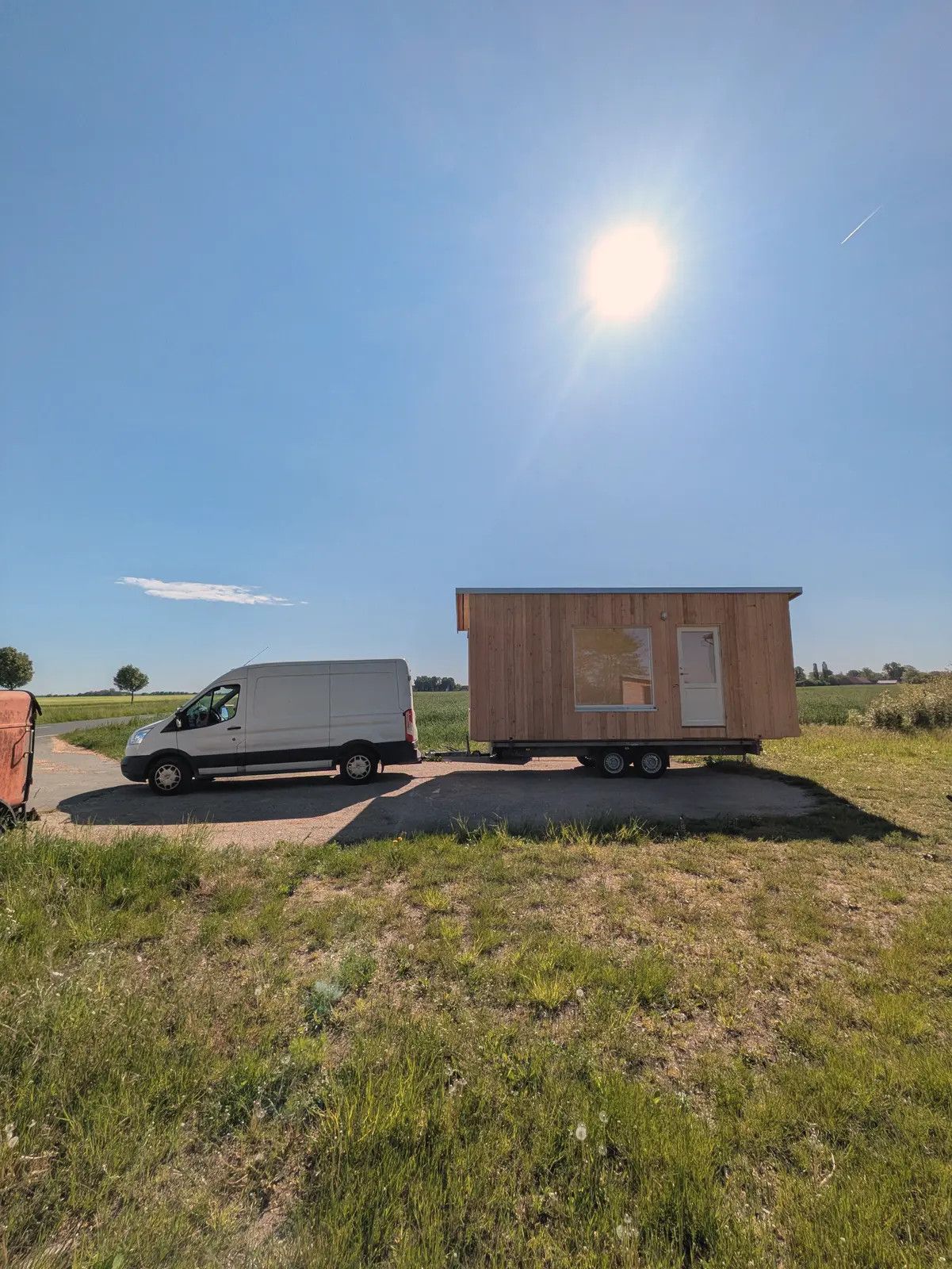 Transporter mit einem LandAnker auf dem Anhänger am Feldrand, darüber die Sonne