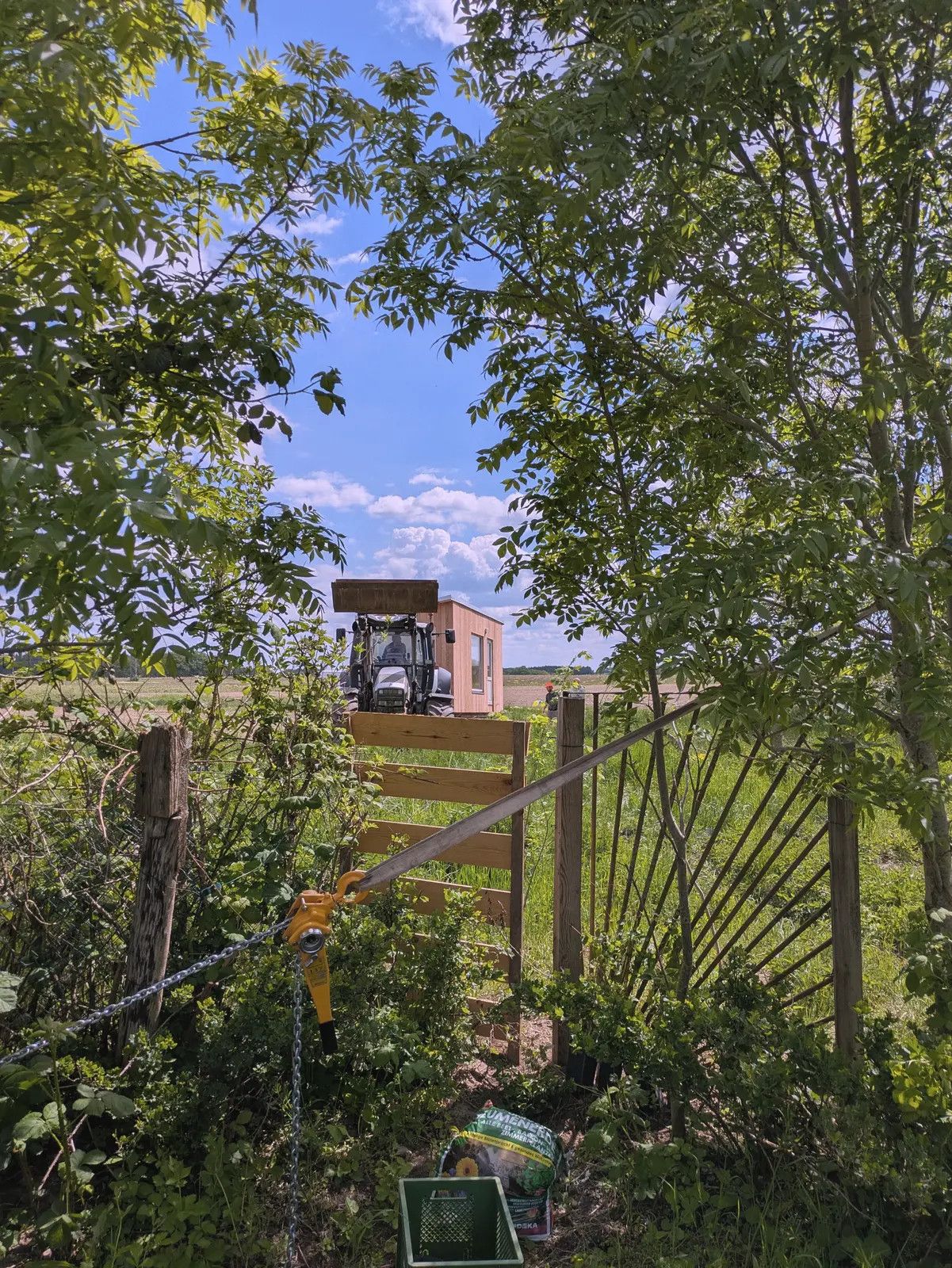 Durch ein Gartentor gesehen: Ein Traktor bringt einen LandAnker über die Wiese