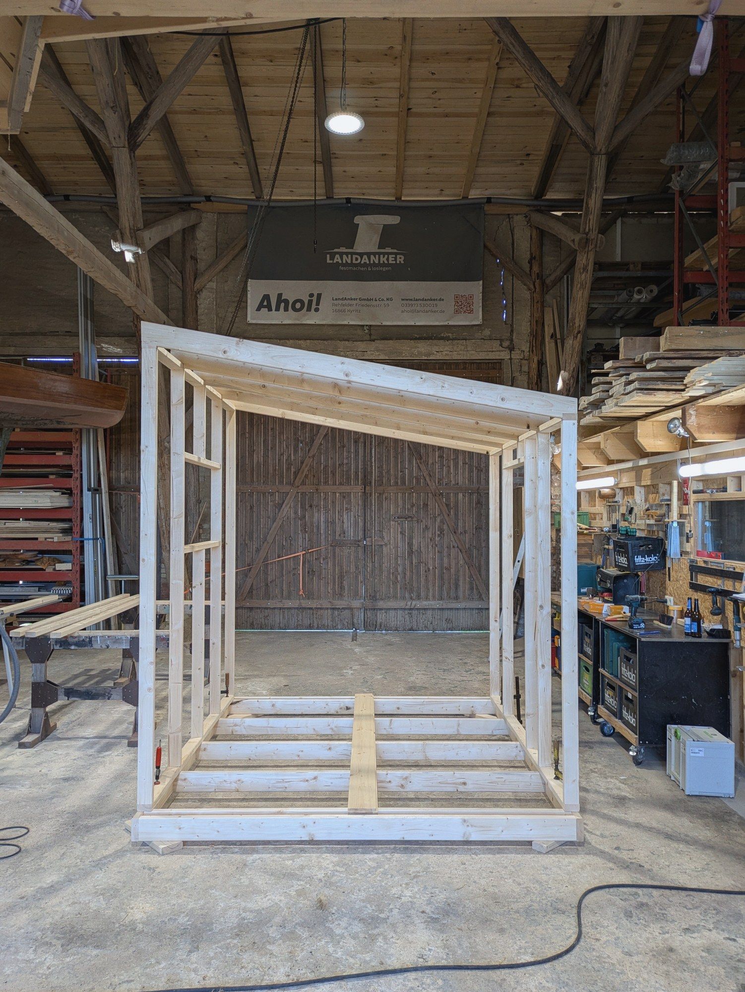 Fertiges Holzständerwerk mit Dachbalken in der Werkstatt, dahinter das geschlossene Scheunentor