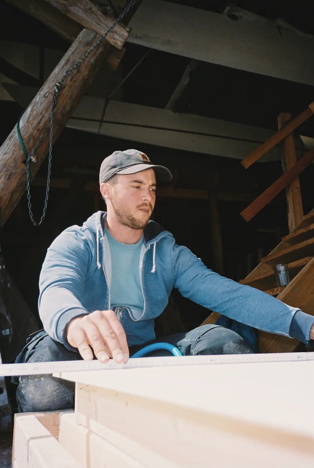 Ein Handwerker mit Basecap misst an einer hellen Holzplatte in der Werkstatt