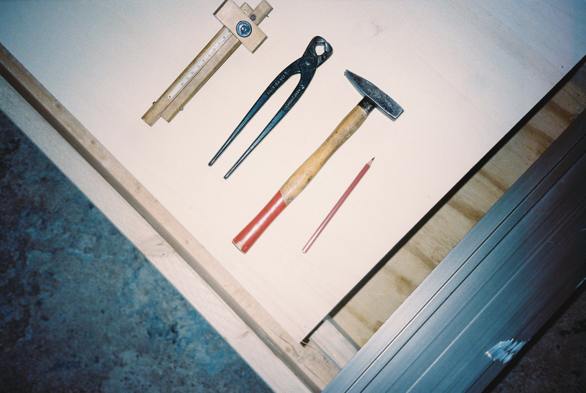 Zollstock, Zange, Hammer und Bleistift auf einer Holzplatte